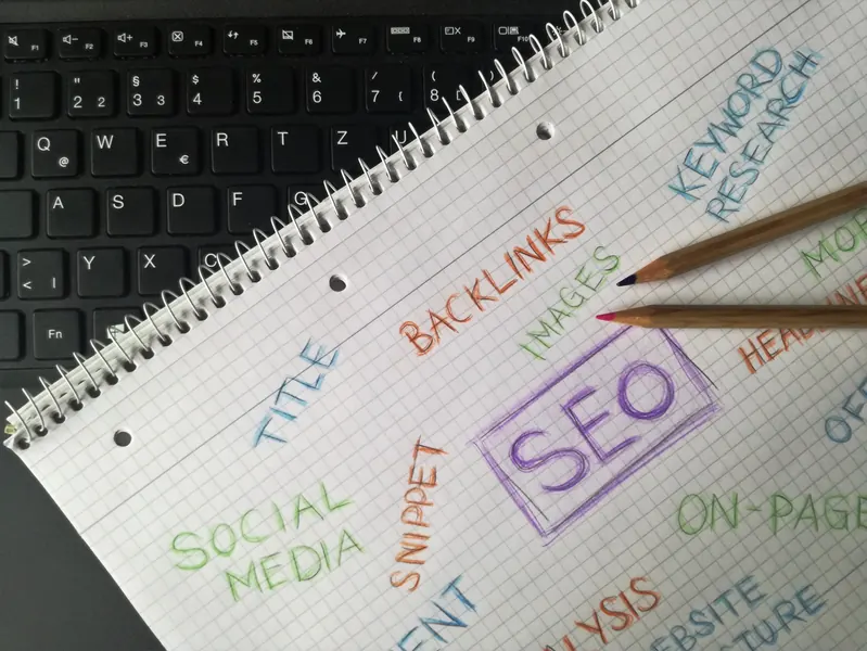 Spiral notebook with SEO, backlinks, keyword research, on-page and title written in colored pencil, next to a keyboard