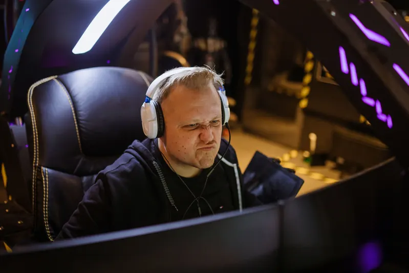 Streamer wearing a headset, concentrating in front of his screens in a purple-lit gaming setup